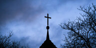 Dunkle Wolken ziehen über das Kreuz auf einer evangelischen Kirche in der Region Hannover hinweg